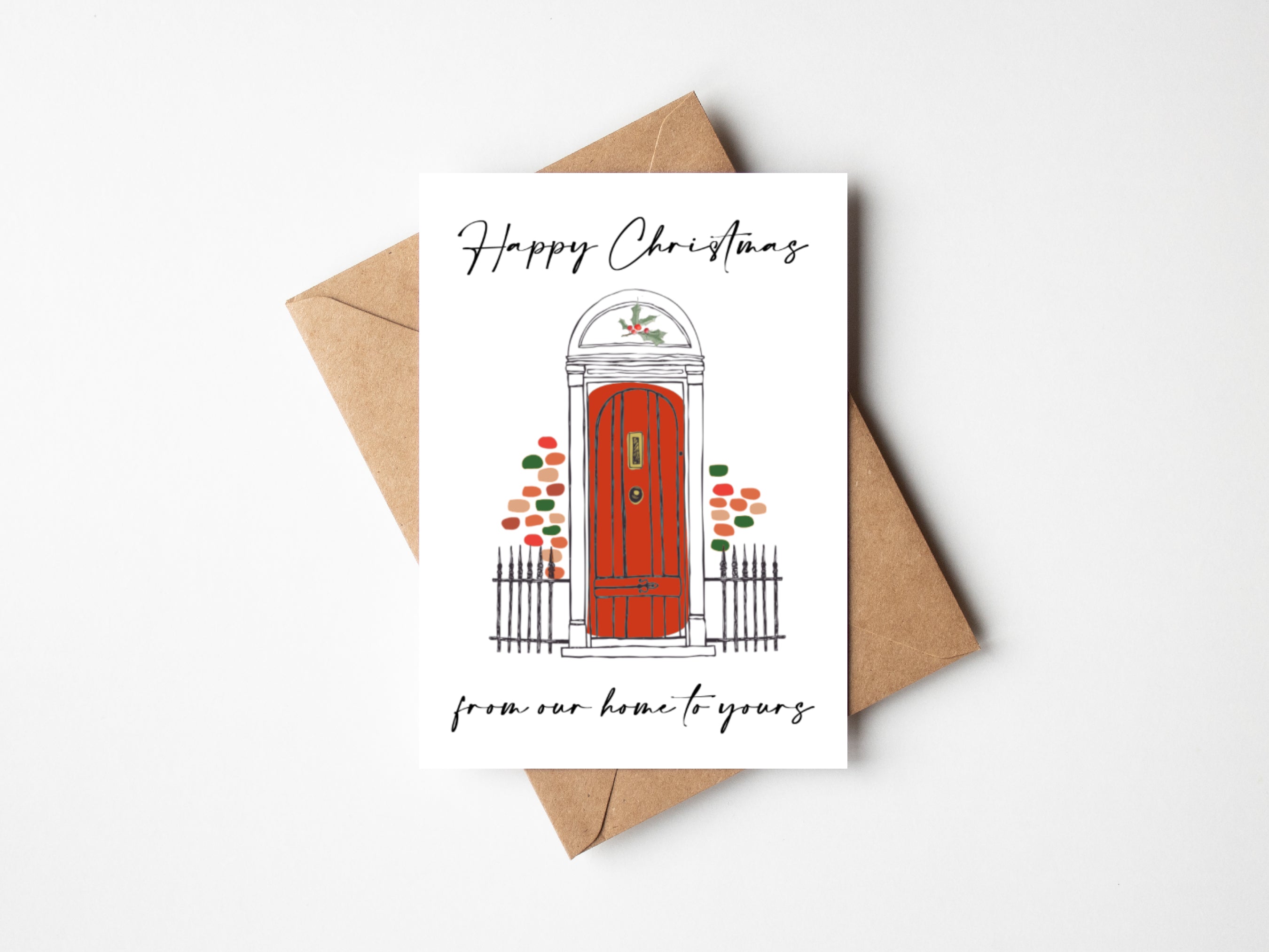 happy christmas from our home to yours card featuring red edwardian door with colourful bricks and holly bush sits on top of brown kraft envelope